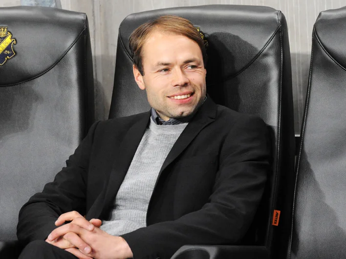 Andreas Alm sitter leende på AIK:s tränarbänk 2013 i mörk kavaj och grå tröja